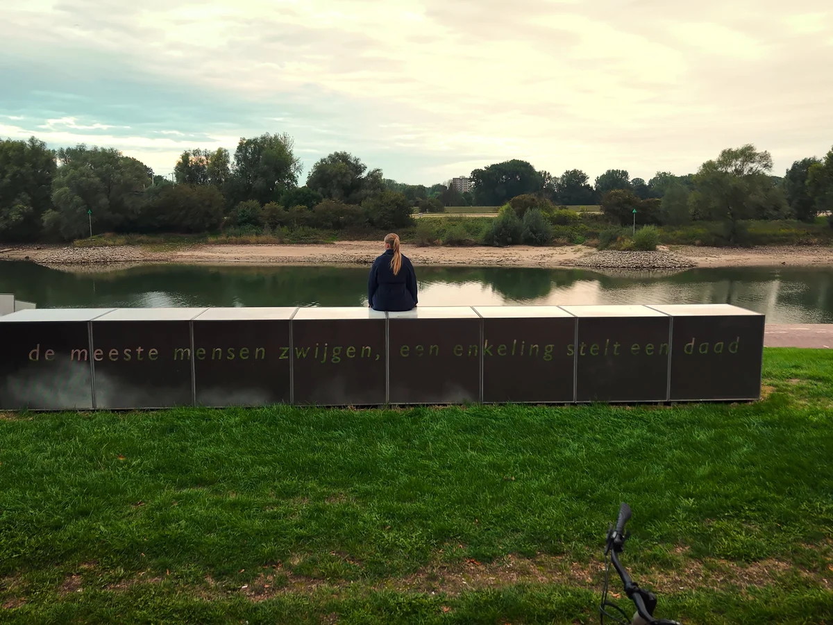 Een vrouw zit aan de Rijn in Arnhem en kijkt uit over het water